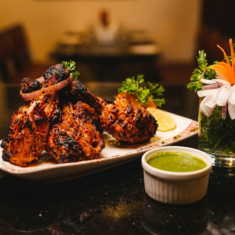Grilled chicken drumsticks with onion, lemon, and parsley, served with a green dipping sauce.