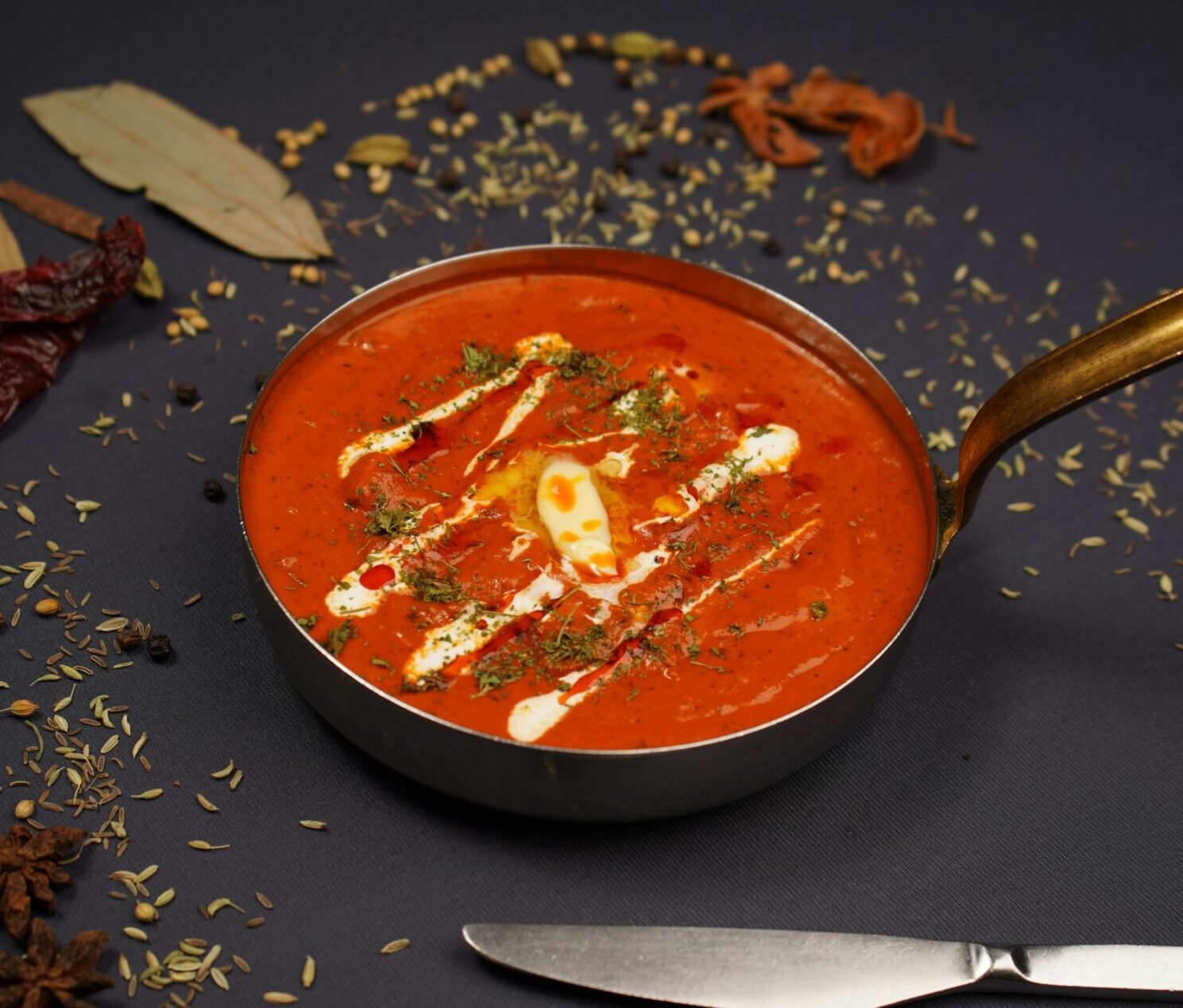 Indian butter chicken served in a pan with scattered spices, showcasing vibrant flavors.
